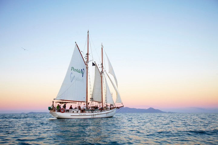 A sailboat on the ocean during sunset with a clear sky and distant hills.