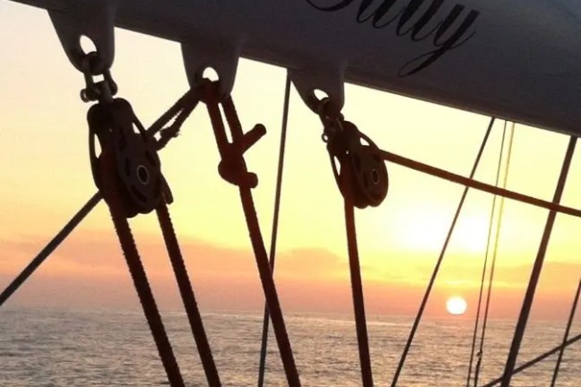 Sailboat rigging at sunset with ocean view, 'Mi' Lady' printed on sail arm.