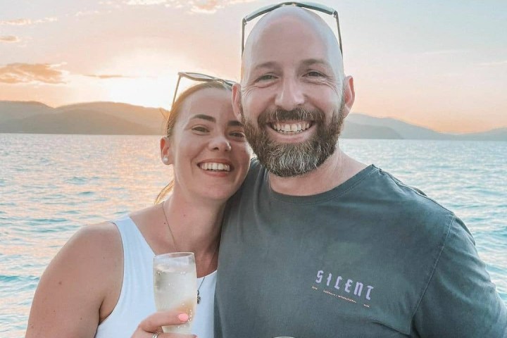 a person holding a wine glass standing next to a body of water