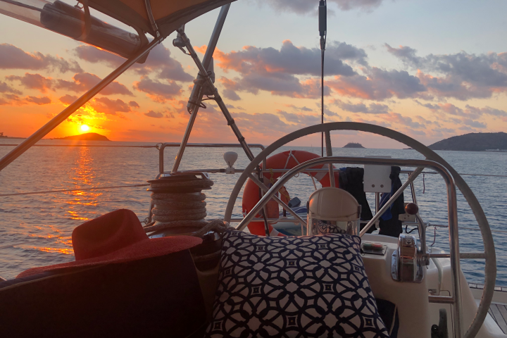 Sunset view from sailboat cockpit with a red hat and patterned cushion.