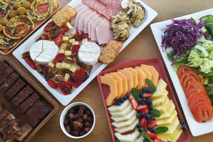 Assorted food platters with meats, cheeses, fruits, veggies, and desserts on a table.
