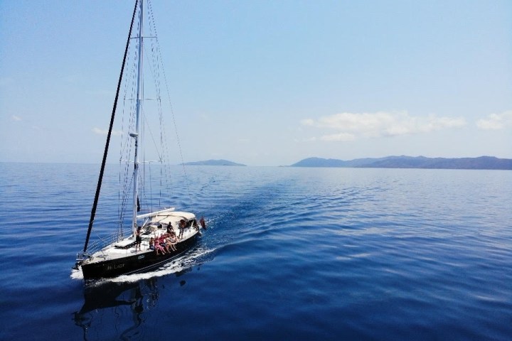 Sailboat on calm blue sea with distant land under clear sky.