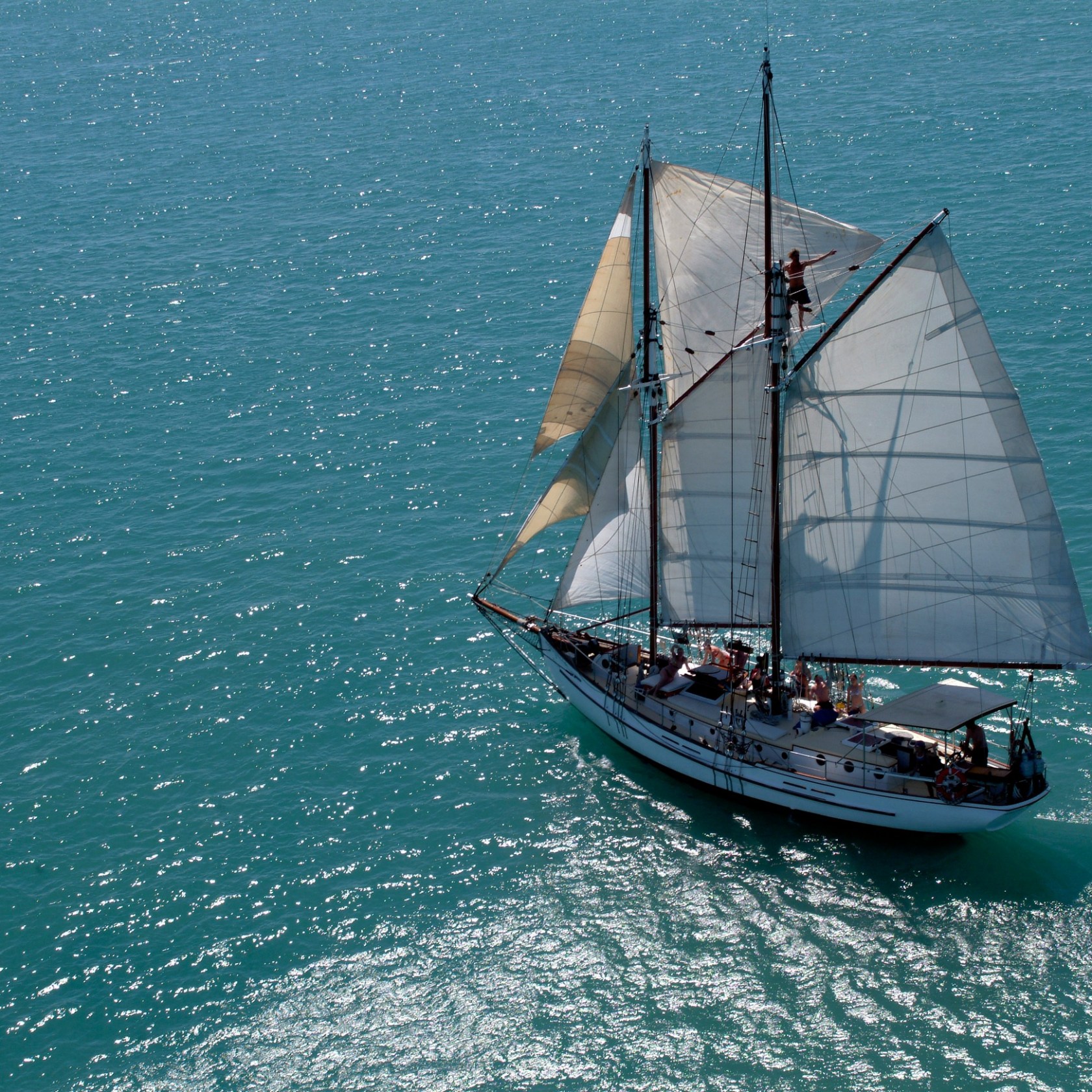 Sailing ship with white sails on bright blue ocean water.
