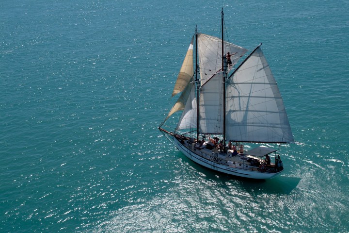 Sailing ship with white sails on bright blue ocean water.